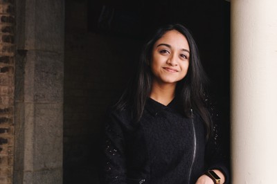 Evani smiling at the camera with a dark background. 