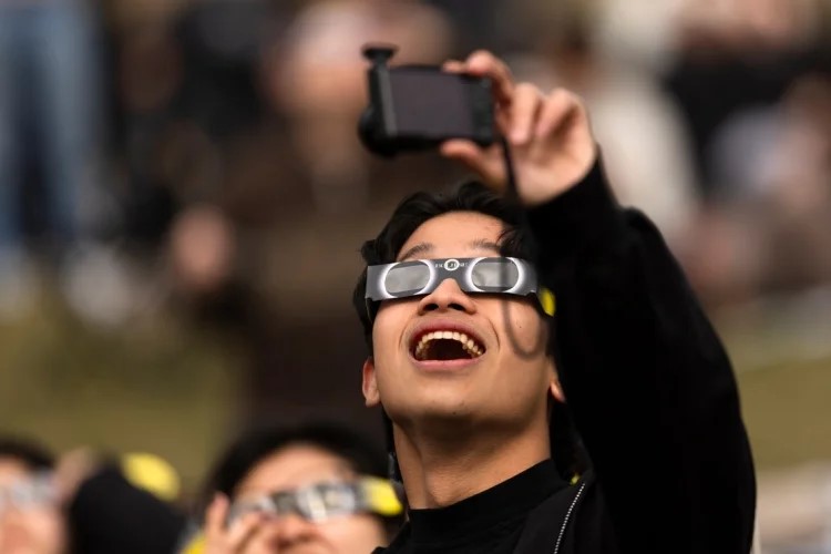 A person looking at the eclipse with protective eyewear and a camera.