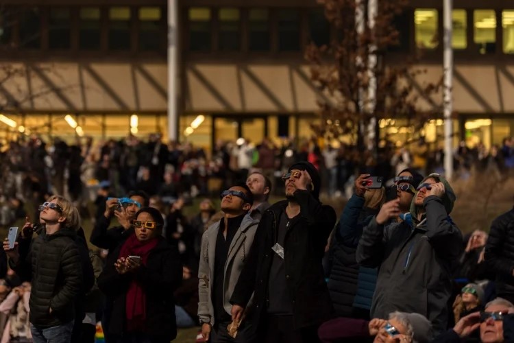 A large group of people looking at the eclipse wearing protective glasses.