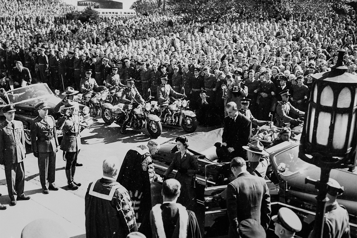 Princess Elizabeth and the Duke of Edinburgh are greeted at Hart House by U of T Chancellor Vincent Massey - a great crowd is shown along with motorcade and military greeting line