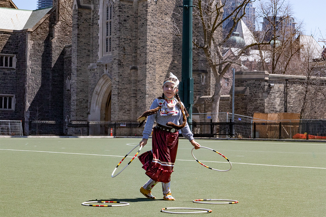 A child holding two hoops with three on the green grass at her feet