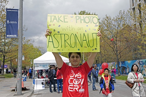 A man holding a sign that says "Take a photo with an astronaut"
