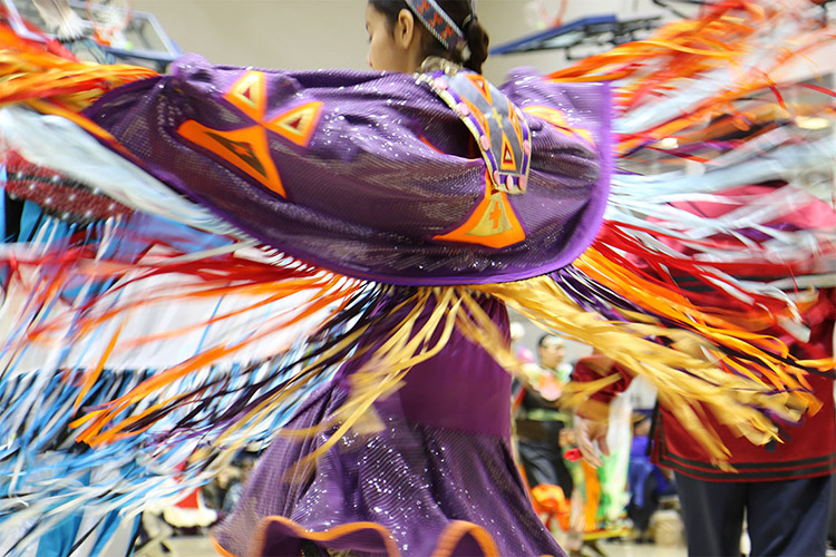 A participate dancing in purple, orange and yellow clothing at the university’s first powwow.