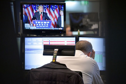 Man holding his head while Donald Trump broadcasts on a television nearby