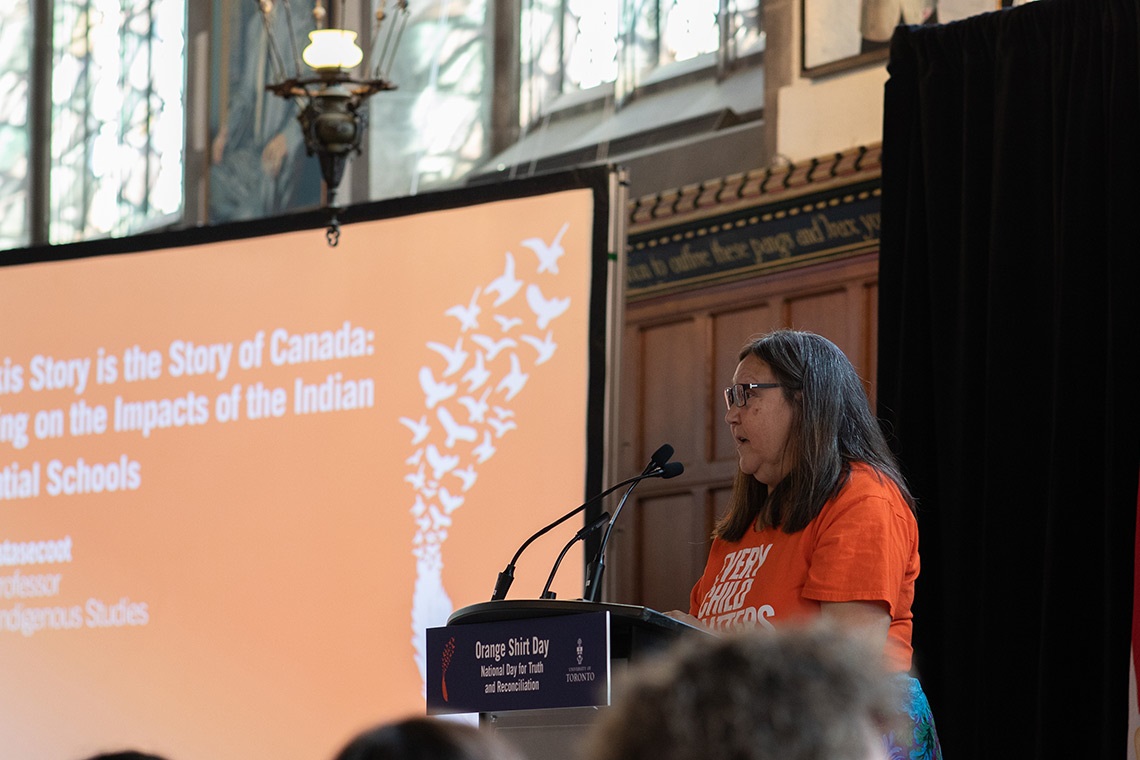 Brenda WastasecooT in an Orange Shirt at a podium