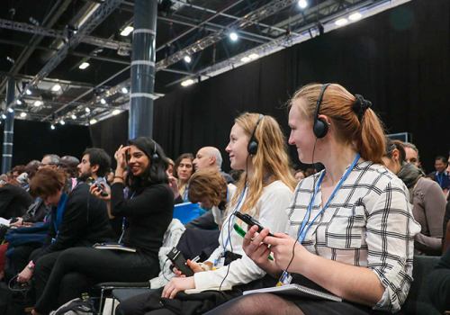 A large group of people sit in a room with headphones.