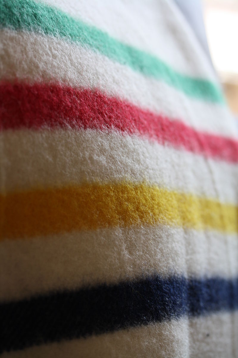 close up of a HBC blanket featuring a green stripe, red stripe, yellow stripe and indigo stripe on a white background