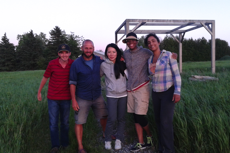 Five students, standing with their arms around each other's shoulders, smile at the camera