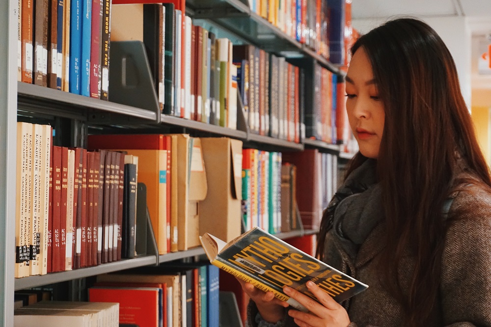 Woman reading a book on mythology in library stacks