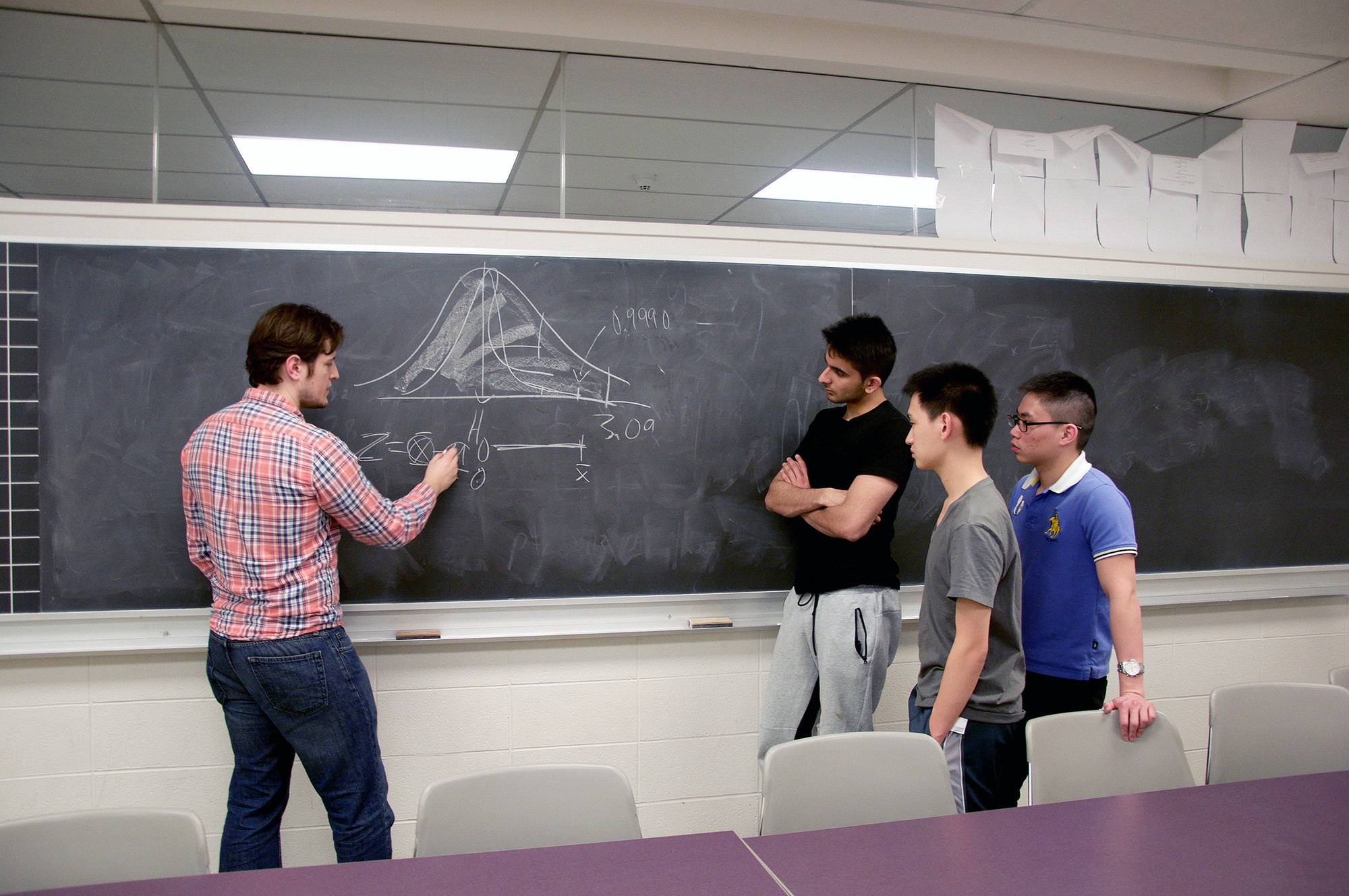 Professor writing an equation on a chalkboard while three students watch