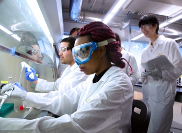 Students in white medical coats conducting an experiment in a lab at U of T.