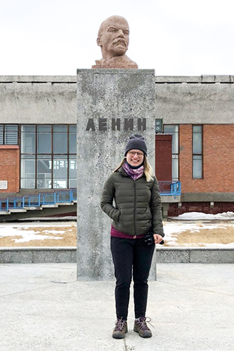 Alina Bykova standing in front of a bust of Lenin on a cold grey day.