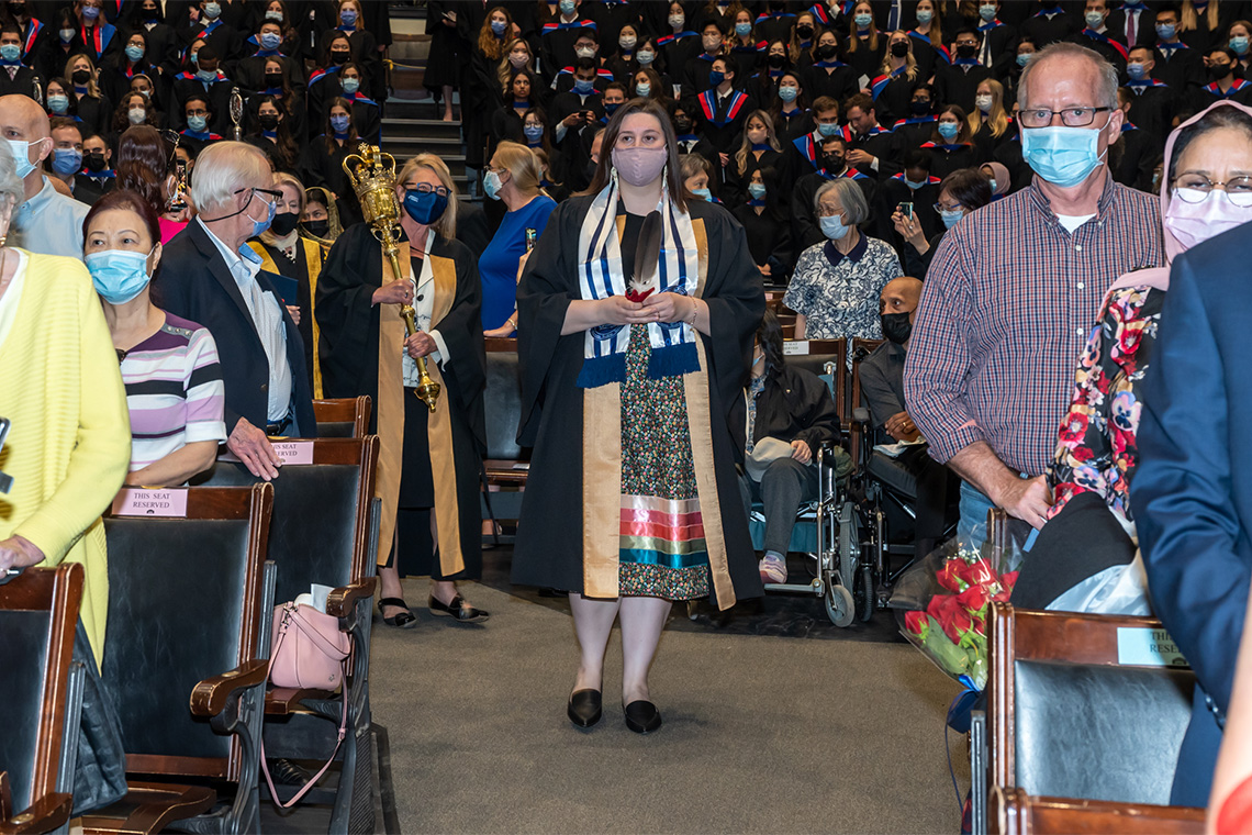 Lindsey Fechtig, manager of the Office of Indigenous Health in the Temerty Faculty of Medicine and U of T's first-ever Eagle Feather Bearer, walks down the aisle at Convocation Hall.