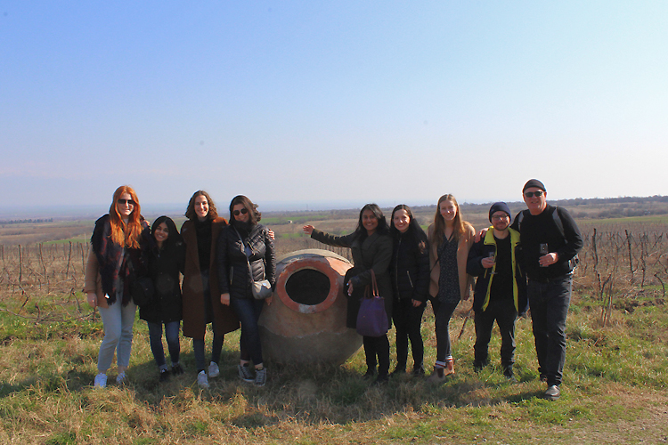 Students and Associate Professor Robert Austin stand in a field in front of a large clay winemaking vessel