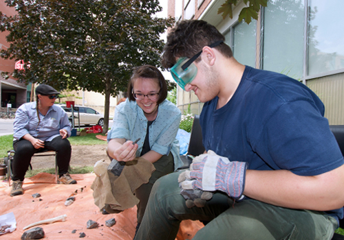 Instructor Emma Yasui shows Patrick Green some features that are typical of stone artifacts during the flint-knapping workshop.