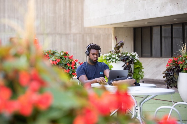 Student typing on a laptop with headphones on, flowers in the foreground