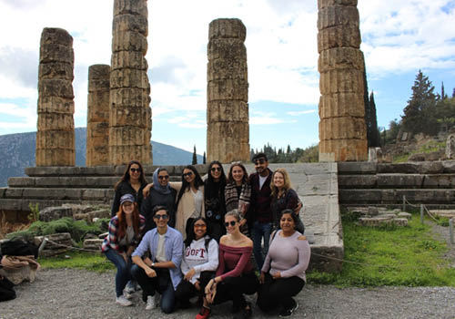 Students pose for a picture in-front of large stone pillars outside in Delphi, Greece.