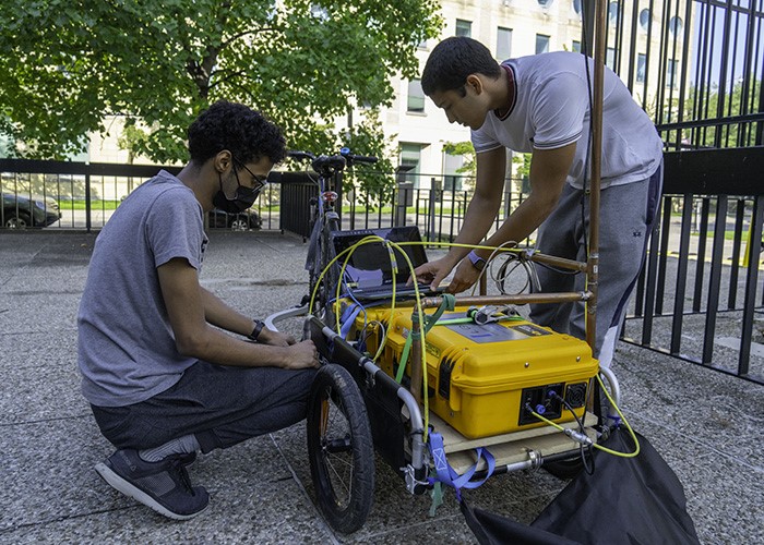 Ibarra Mendez (r.) and Kandapath (l.) working on a yellow piece of equipment with wires.