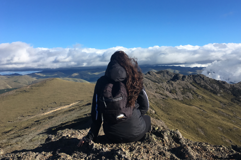 A student sitting at the top of a mountain peak, looking away from the camera