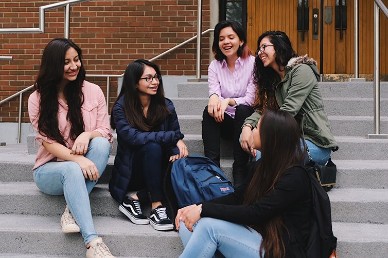 Karol and friends chatting on outdoor steps of a building on campus