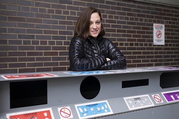 Kim Slater posing behind a recycling, garbage and compost bin
