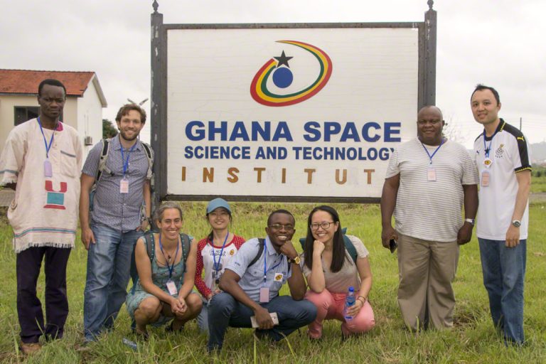 Patrice Okouma, Wesley Cheek, Linda Strubbe, Meiling Deng, Sudum Esaenwi, Jielai Zhang, Romanus Eze, Thai Duy Cuong Nguyen standing in front of the Ghana Space Science and Technology Institute sign.