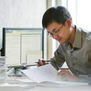 A person sitting at a computer looking at paperwork.