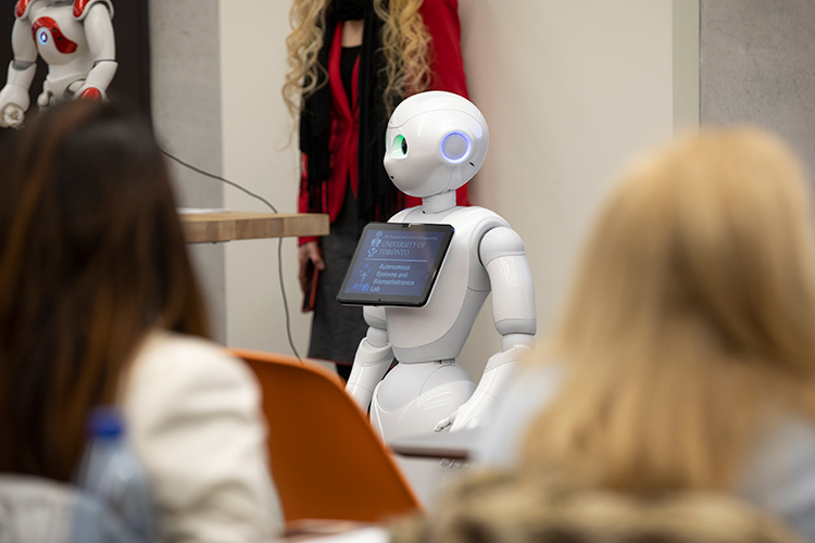 A white humanoid robot at the front of a room of people