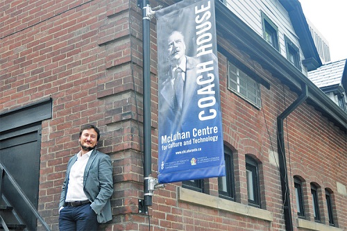 Paolo Granata standing against a brick wall beside a blue and grey outdoor banner that says, "Coach House."