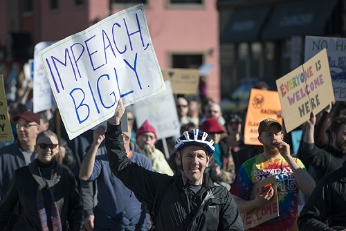 A protester in a crowd holding up a sign that says "Impeach, Bigly"