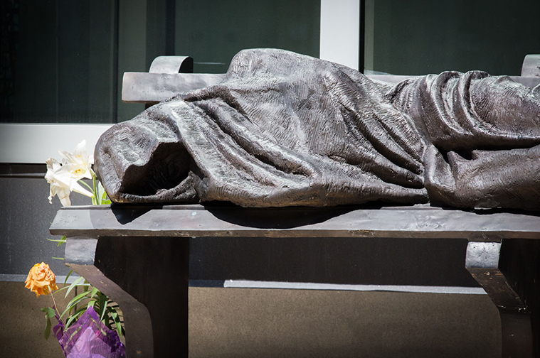 Statue of a homeless person lying on a bench