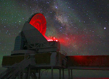 A large telescope with a red light beaming through a night sky.