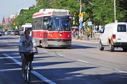 A red and white Toronto streetcar, and a cyclist on a busy summer day.