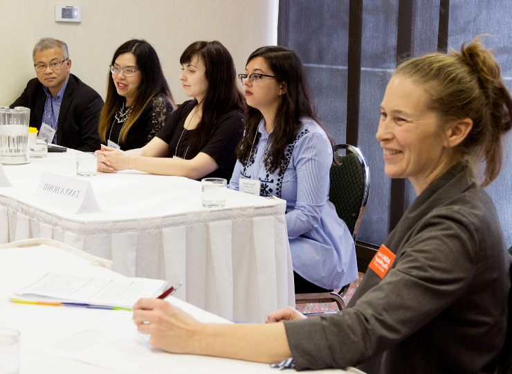 A person sits and smiles on a panel of people at a desk.