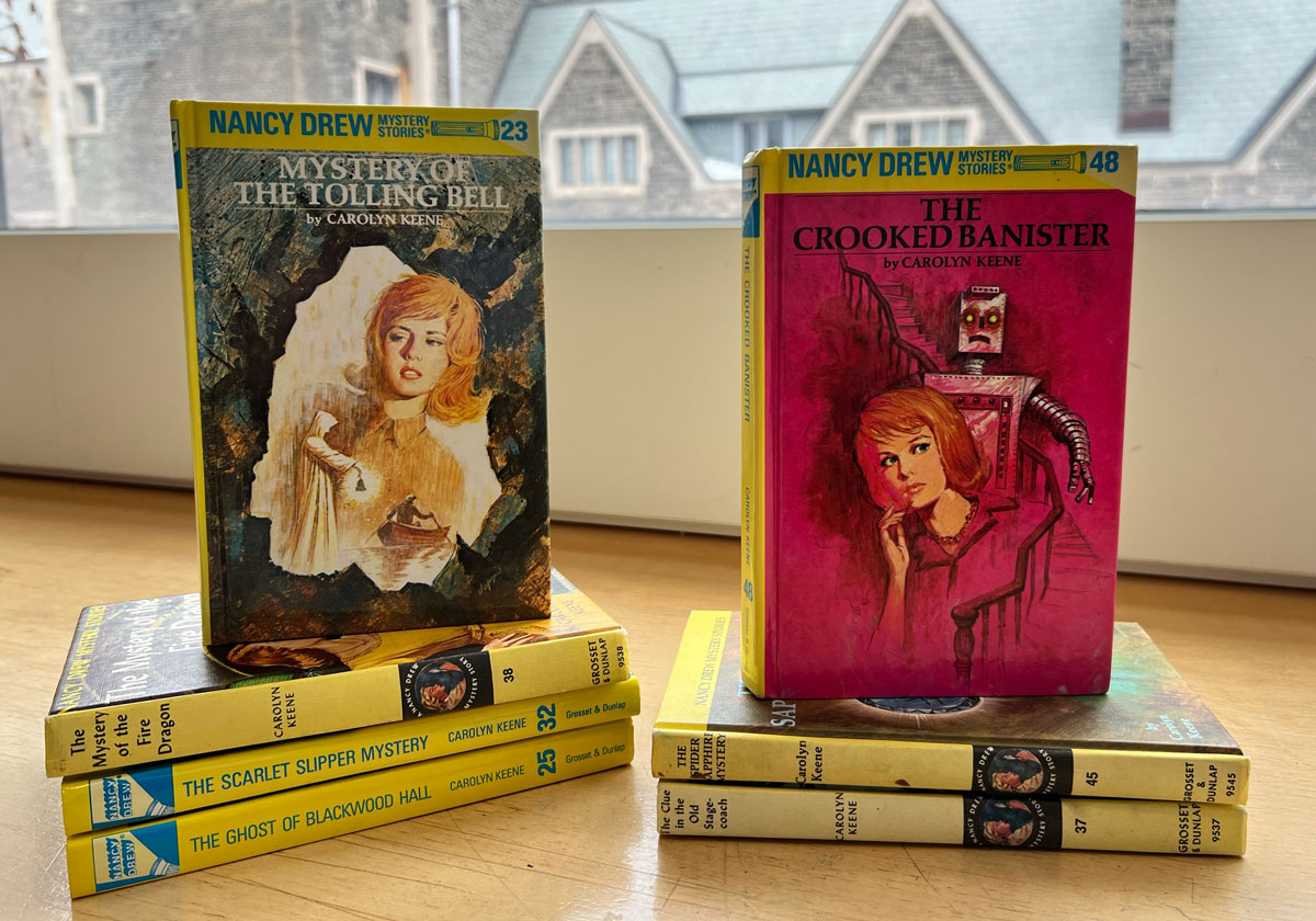 Multiple Nancy Drew books stacked, including, "Mystery of the tolling bell" and "The crooked banister."