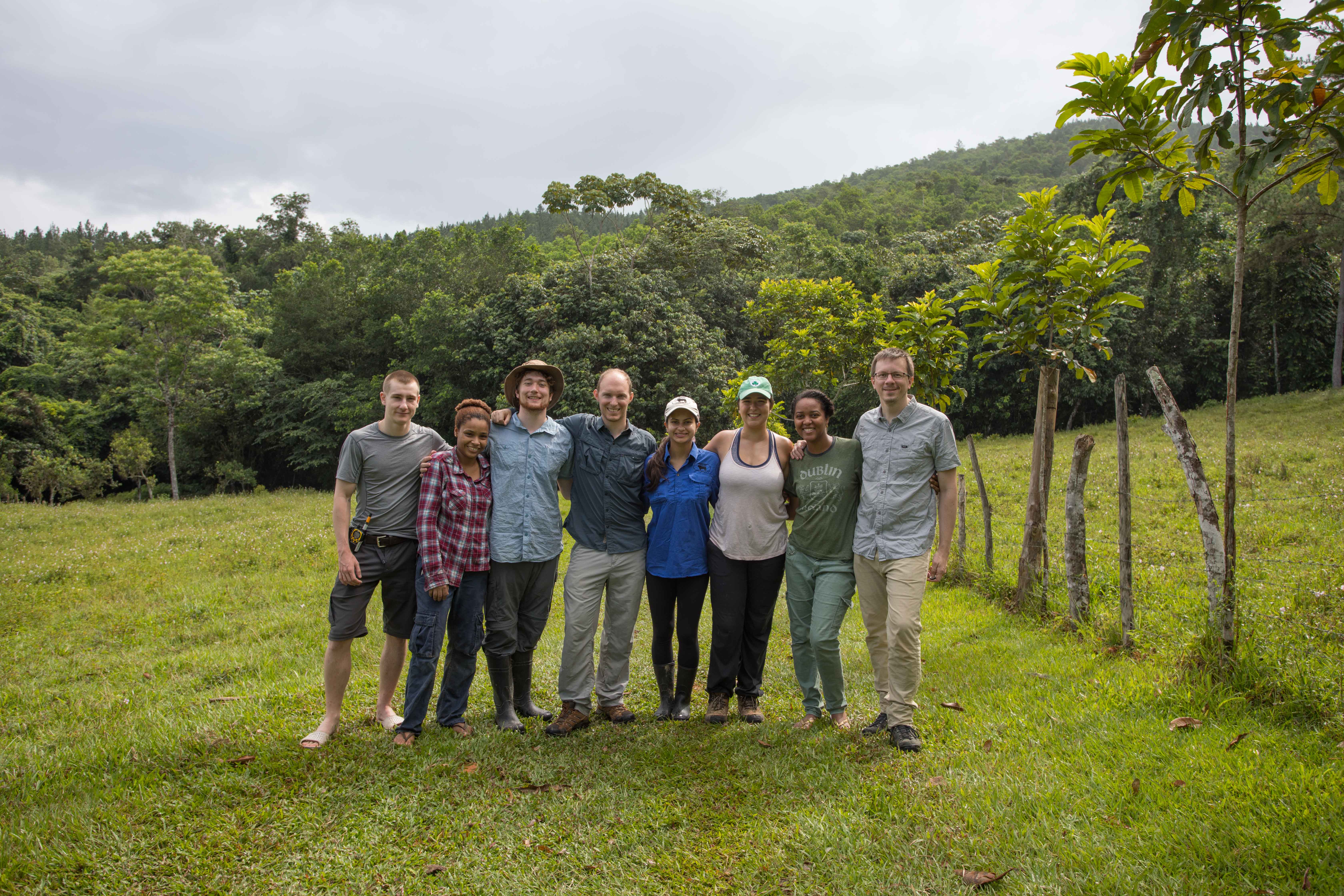 Eight people posing in a green field with trees in background