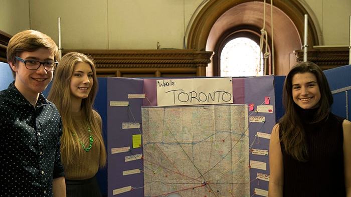 Three students standing in front of poster board titled "Who is Toronto?"