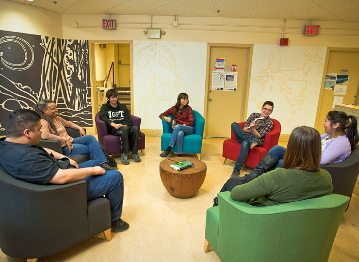 Students gather in a circle of chairs in a room.