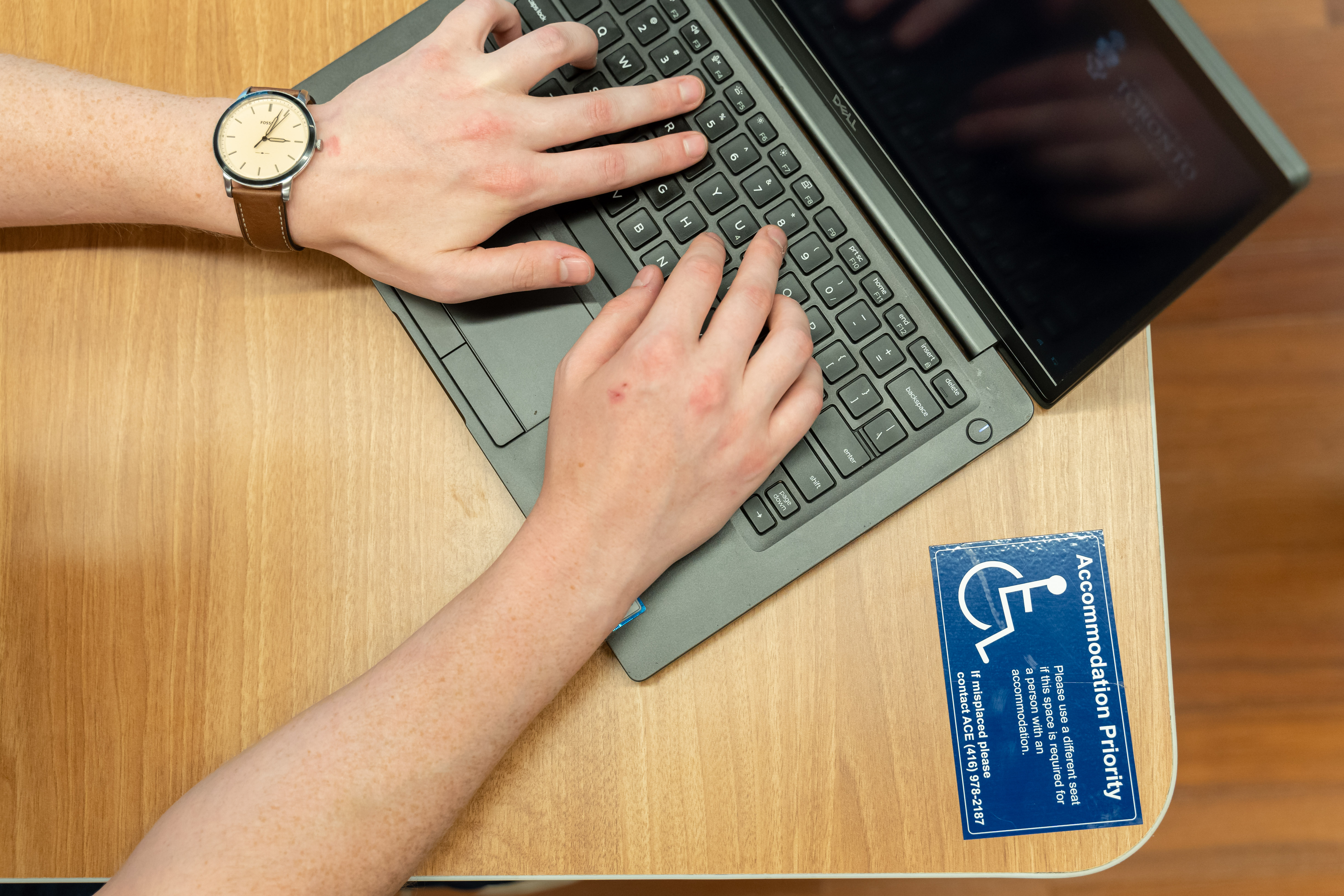 Overhead shot of hands on a laptop with an Accommodation Priority sticker on the desk