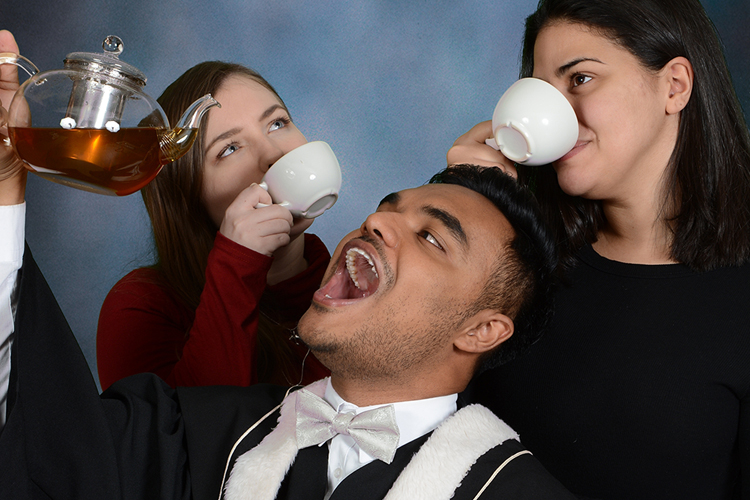 Al-amin Ahamed hoists a glass teapot overhead while two friends sip tea from white mugs