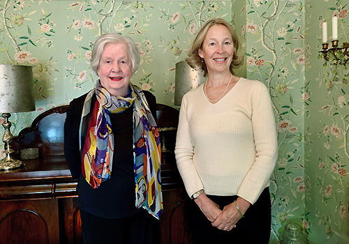 Alice and Katie Lundon standing inside a room with green floral wallpaper