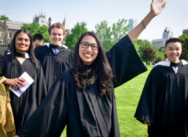 A student excited to graduate with fellow new Alumni outside Convocation Hall on a sunny day.