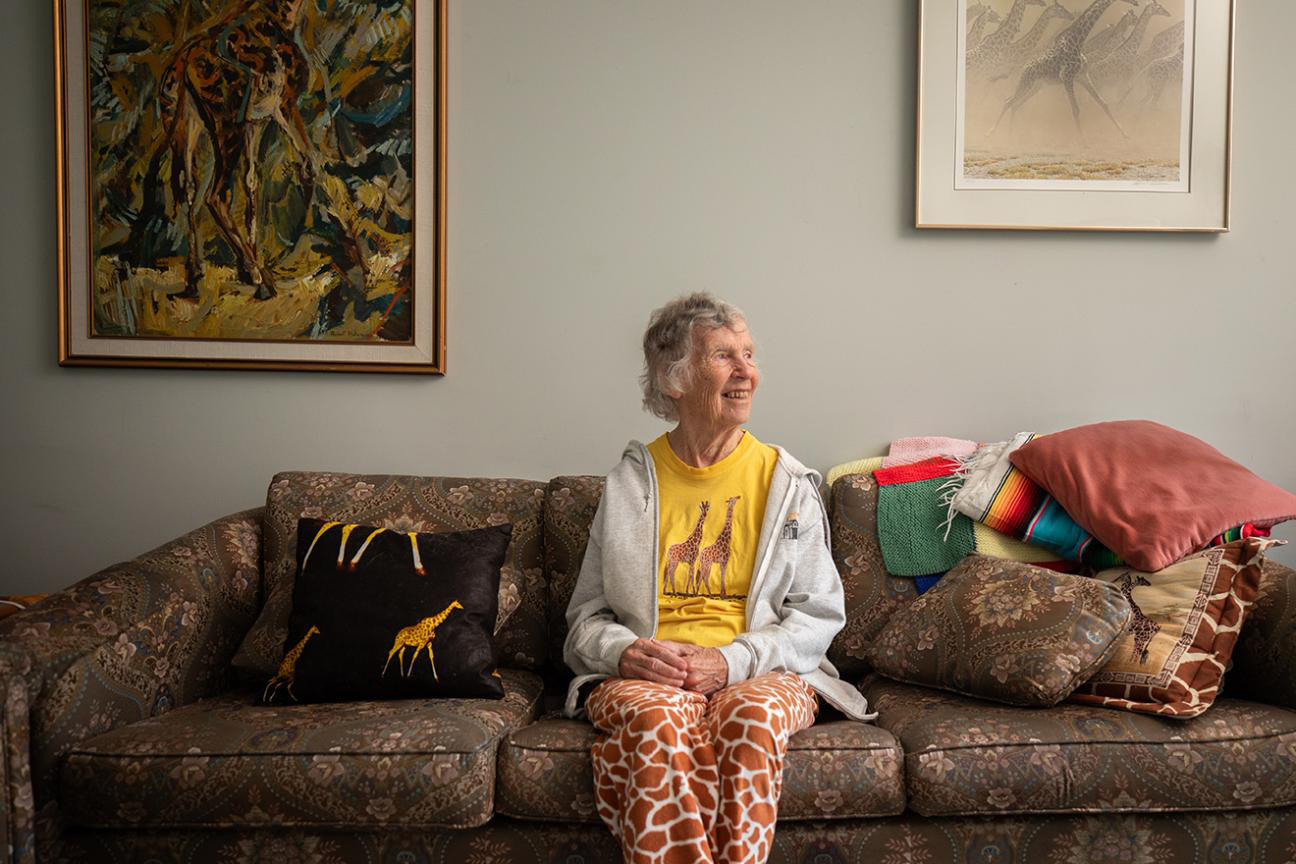 Anne Innis Dagg sitting on a sofa with blankets and a giraffe-print pillow and a wearing giraffe-print pants 