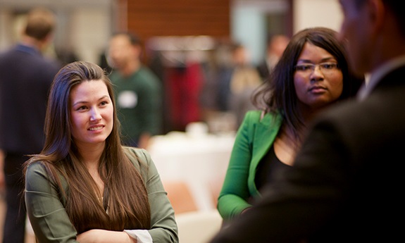 Two students listen to someone speak at a networking event