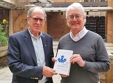 David Cameron and Robert Vipond holding a book between them. Standing outdoors.