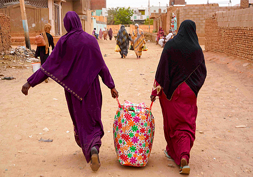 Women carrying belongings walk down a street