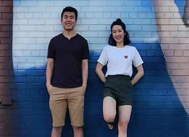 Chan and Li standing against a wall mural with painted hands