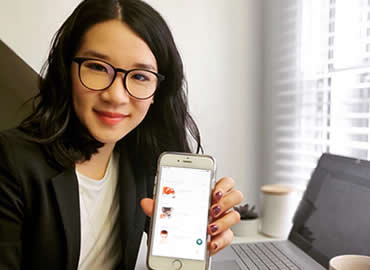 Catherine Chan holding a cell phone with the app on it