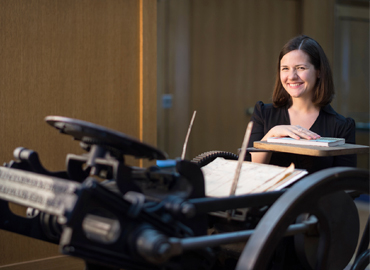 Claire Battershill standing behind a black metal letterpress