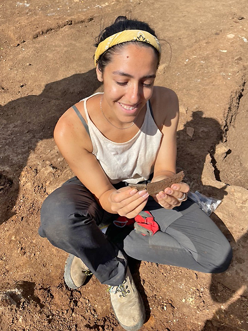 Claudia Paparella holds a yet to be dated fragment of glass as she sits in a trench